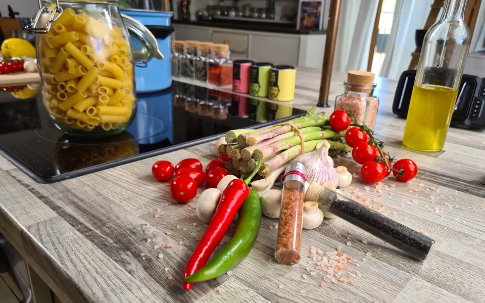 Pasta, asparagus, tomatoes and other ingredients arranged on the kitchen worktop
