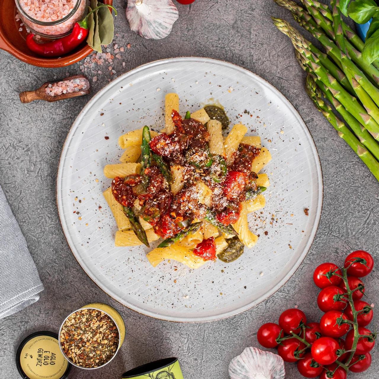 Overhead view of pasta with tomatoes and green asparagus, surrounded by ingredients and Just Spices seasonings